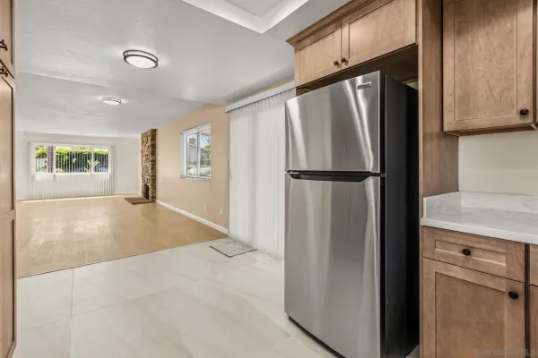 a view of a refrigerator in kitchen and an empty room with wooden floor windows