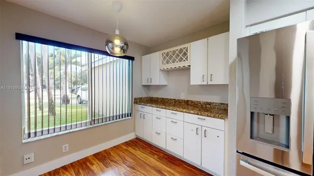 a kitchen with stainless steel appliances granite countertop a refrigerator a oven and white cabinets with wooden floor