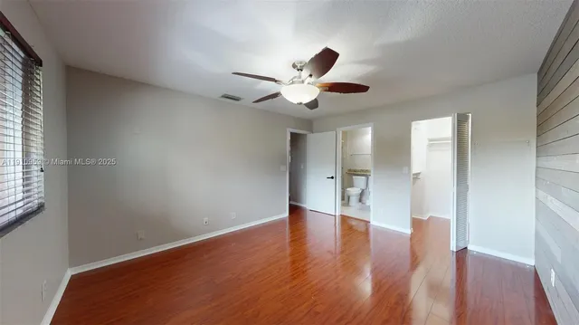 a view of an empty room with wooden floor and a ceiling fan