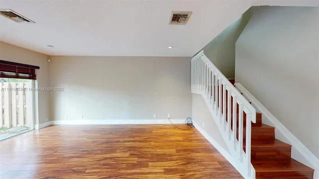 a view of an empty room with wooden floor and stairs