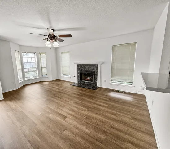 a view of an empty room with wooden floor fireplace and a window