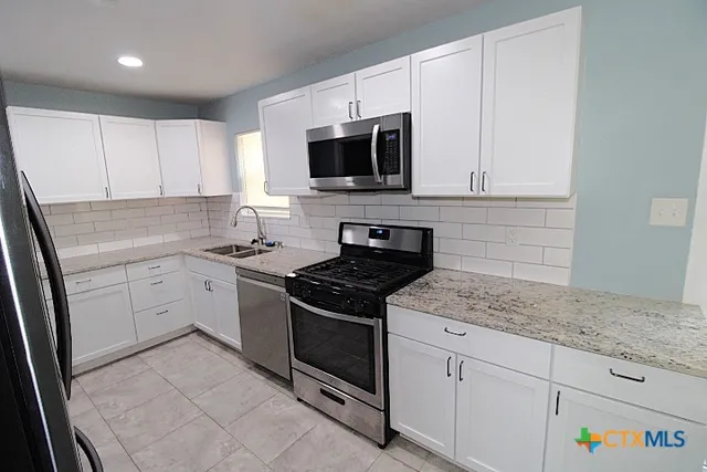 a kitchen with granite countertop white cabinets stainless steel appliances and a sink