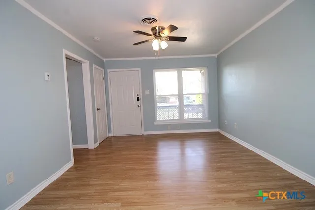 a view of an empty room with wooden floor and a window