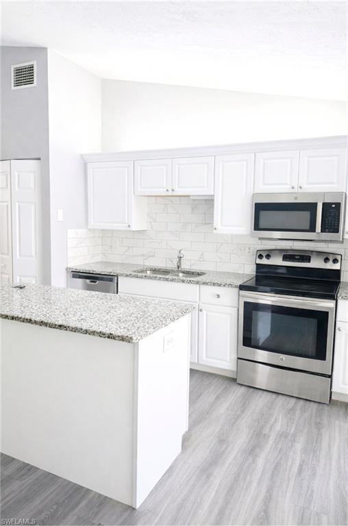 5364 16th Place Southwest, Unit H3 Naples, FL 34116 - Photo 3 of 8 Kitchen with lofted ceiling, white cabinetry, appliances with stainless steel finishes, tasteful backsplash, and light stone counters