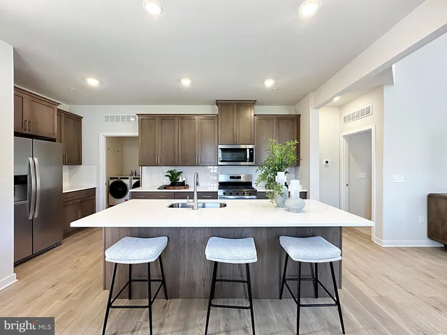 a kitchen with stainless steel appliances kitchen island granite countertop a dining table chairs refrigerator sink and cabinets