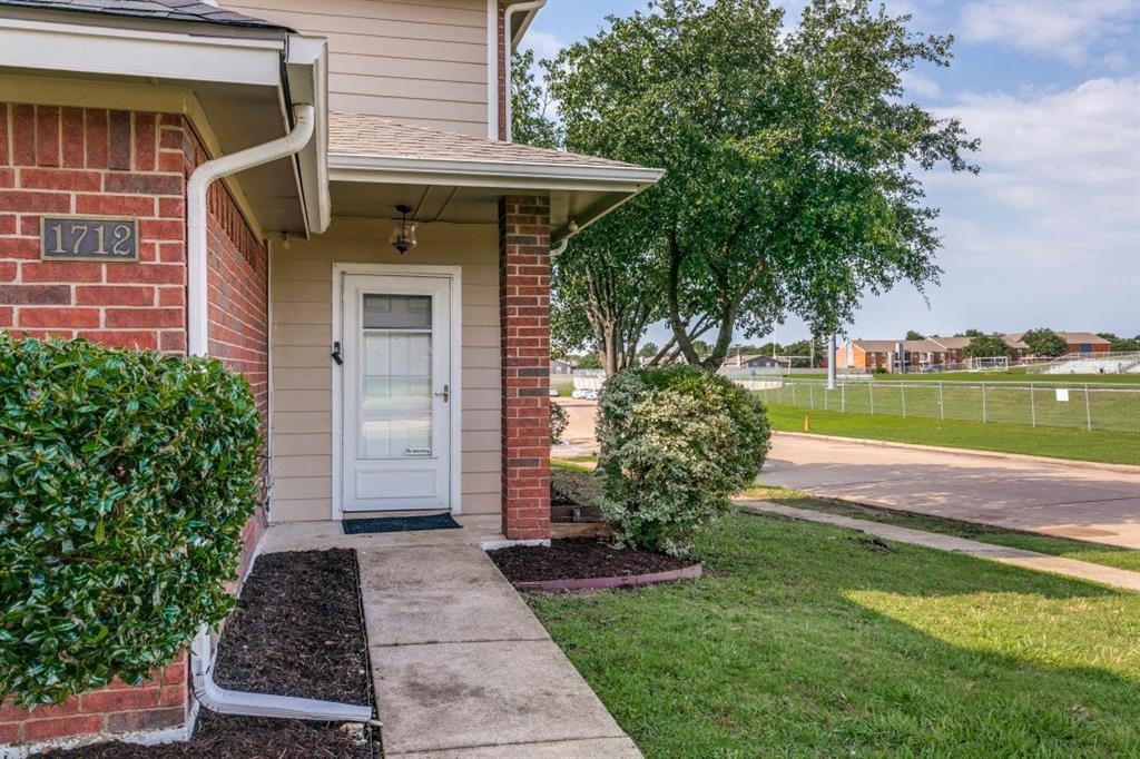1712 East Peters Colony Road Carrollton, TX 75007 - Photo 3 of 25 Exterior featuring red brick and tan siding, covered entry, white door with glass insert, concrete walkway, and established landscaping