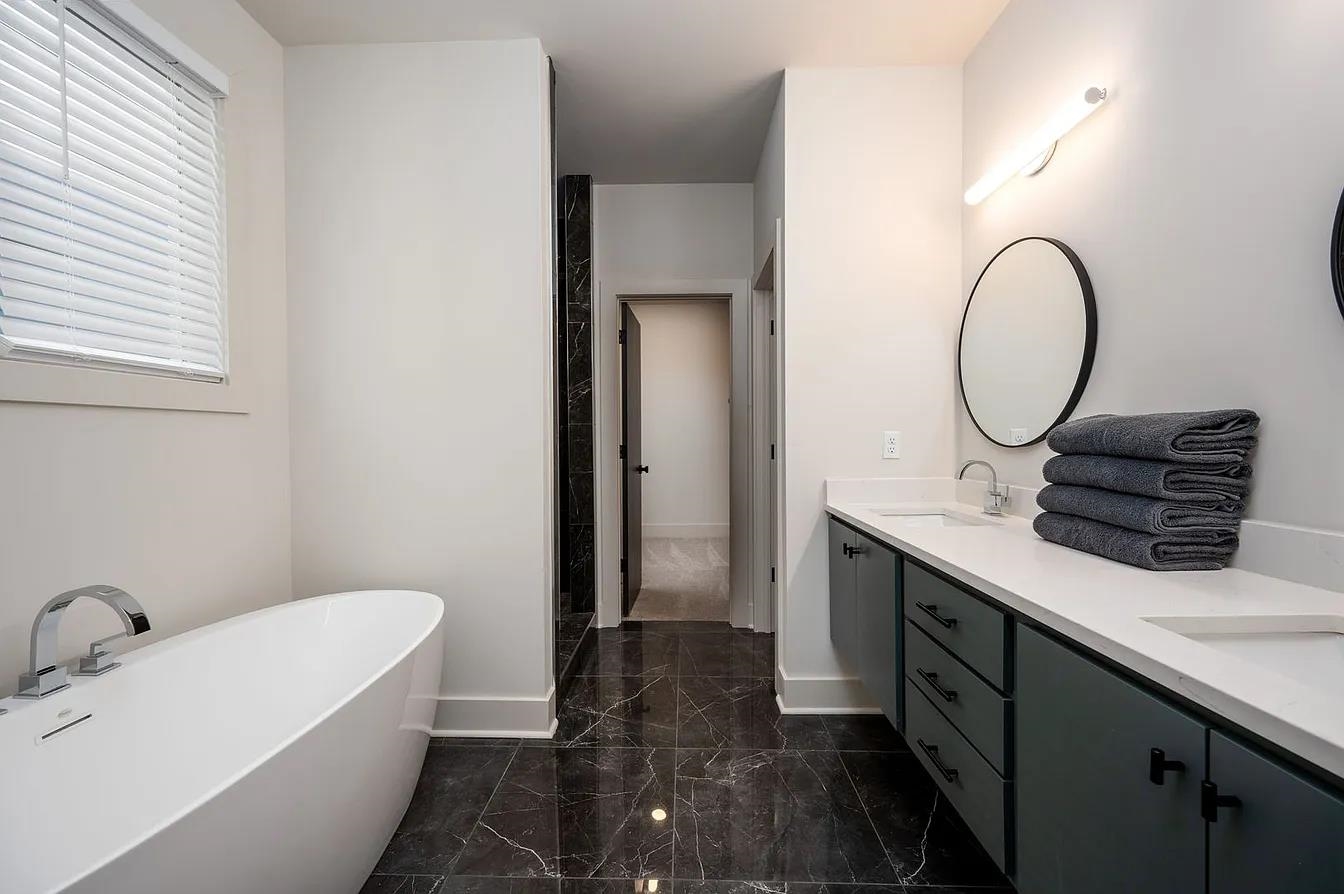 752 Meda Street Memphis, TN 38104 - Photo 6 of 18 Bathroom featuring a freestanding soaking tub, dual vanity with undermount sinks, stone-look tile flooring, and a round wall-mounted mirror