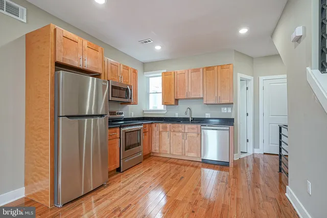 a kitchen with granite countertop stainless steel appliances a refrigerator cabinets and wooden floor