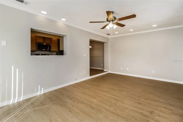 a view of an empty room with wooden floor and a ceiling fan