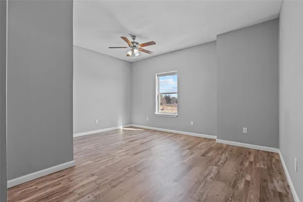 an empty room with wooden floor chandelier fan and windows