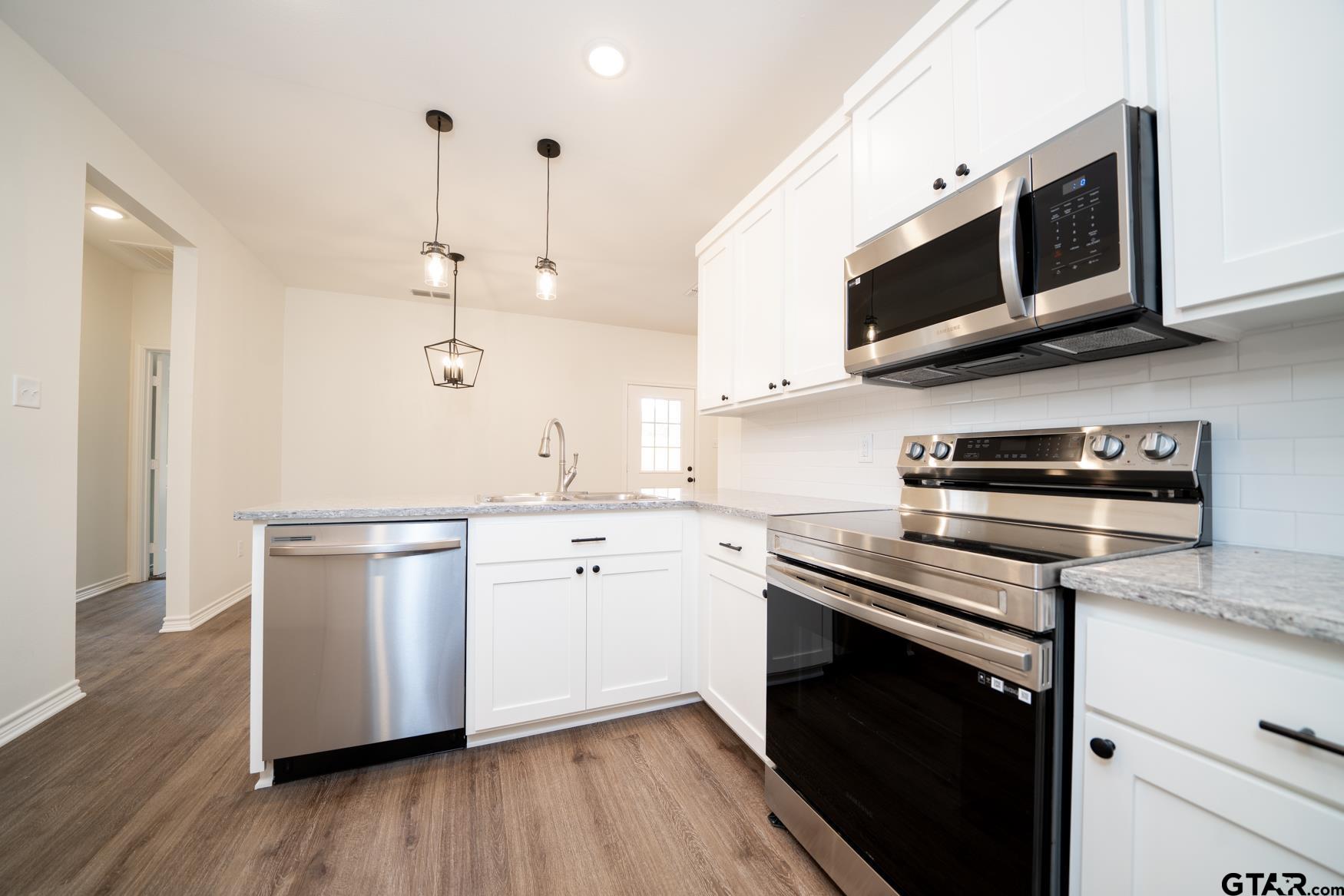 309 Stevens Street Gilmer, TX 75645 - Photo 11 of 28 a kitchen with stainless steel appliances kitchen island granite countertop a stove a microwave and wooden floors