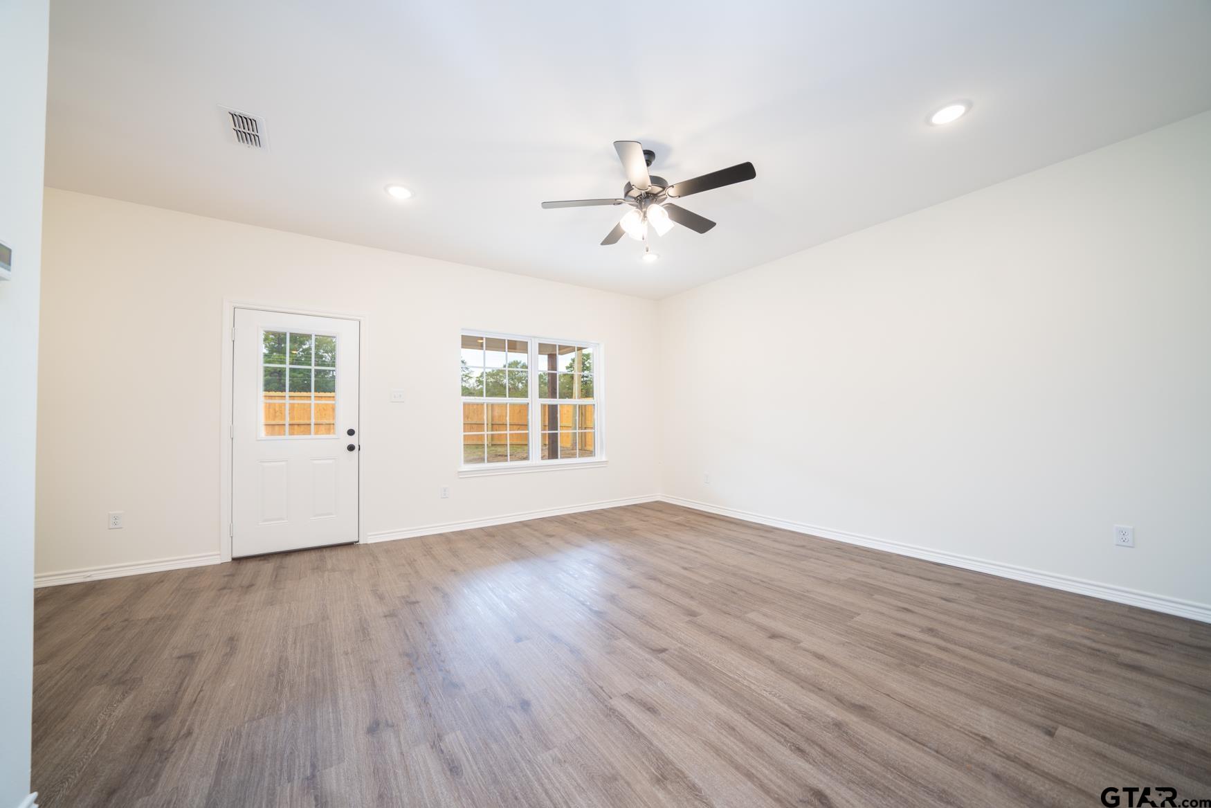 309 Stevens Street Gilmer, TX 75645 - Photo 3 of 28 an empty room with wooden floor ceiling fan and windows