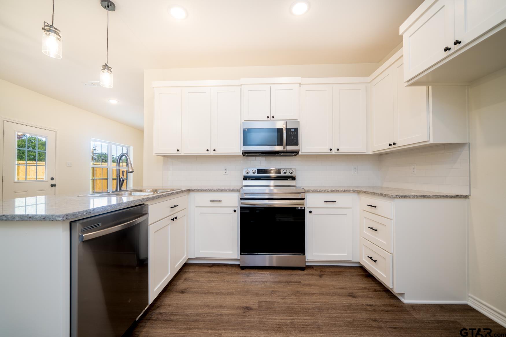 309 Stevens Street Gilmer, TX 75645 - Photo 10 of 28 a kitchen with stainless steel appliances granite countertop a stove top oven a sink and white cabinets