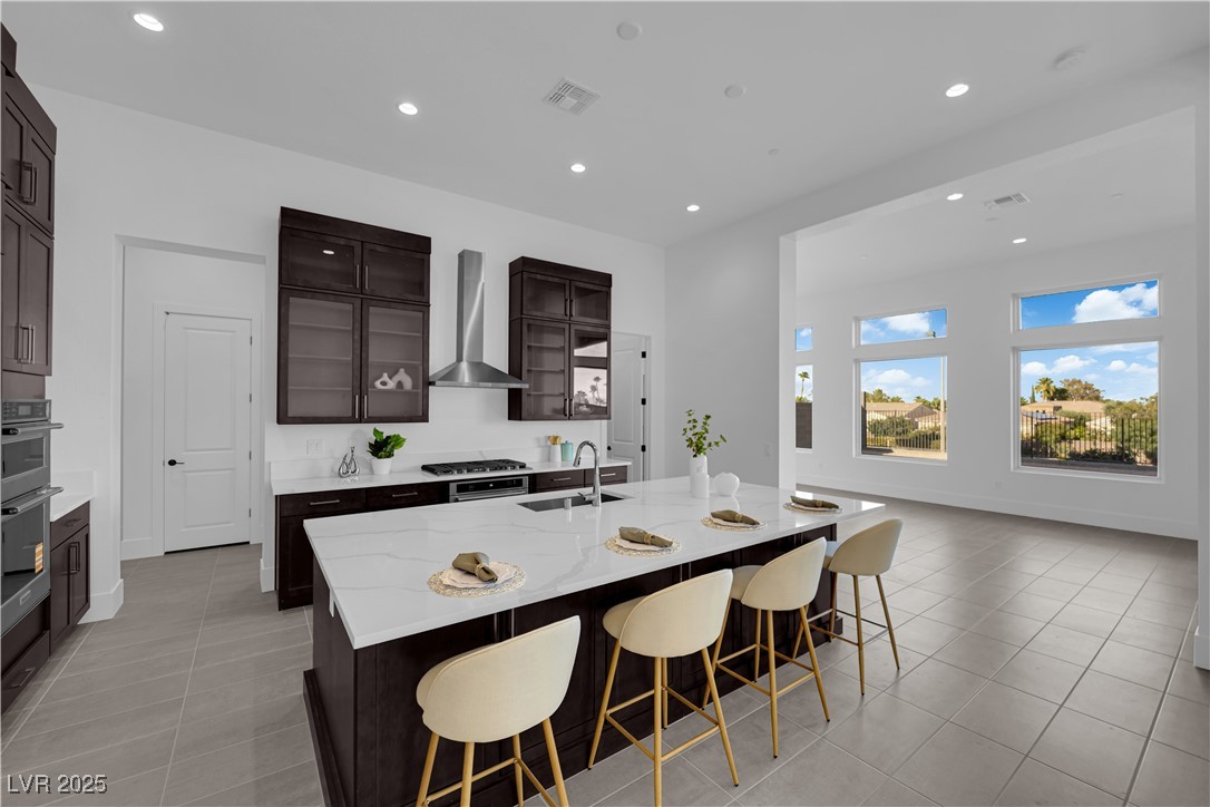 4792 Outlook Peak Street Las Vegas, NV 89135 - Photo 12 of 56 Kitchen with glass insert cabinets, recessed lighting, a breakfast bar area, light stone countertops, and dark brown cabinetry