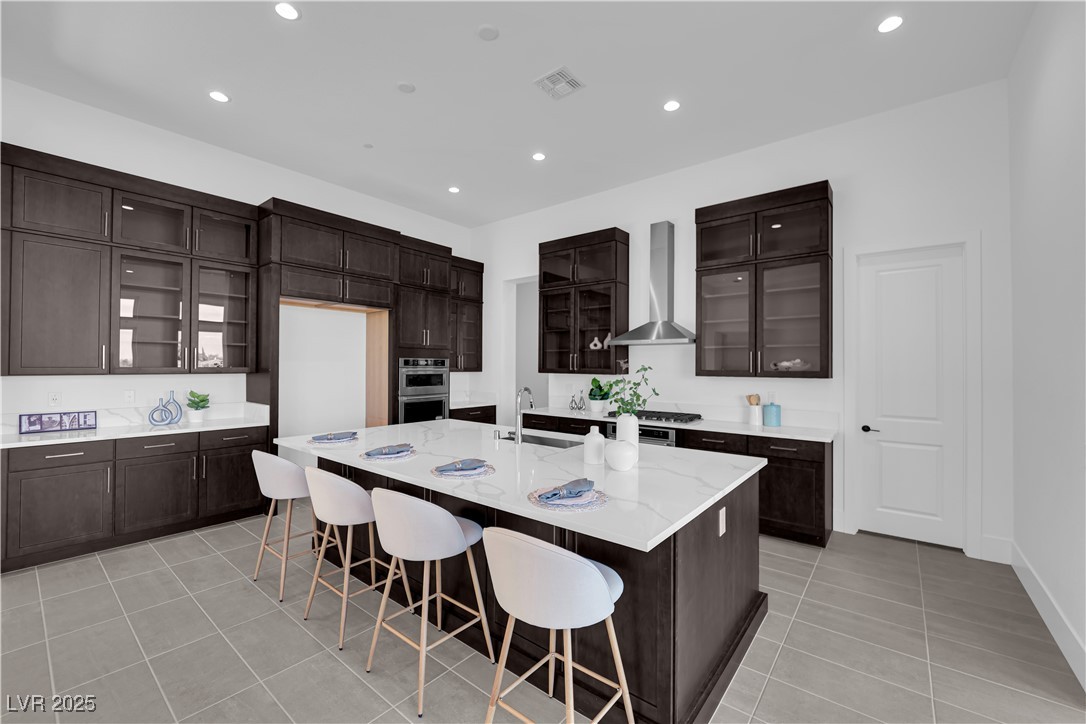 4792 Outlook Peak Street Las Vegas, NV 89135 - Photo 13 of 56 Kitchen featuring glass insert cabinets, dark brown cabinets, a kitchen breakfast bar, recessed lighting, and light stone countertops