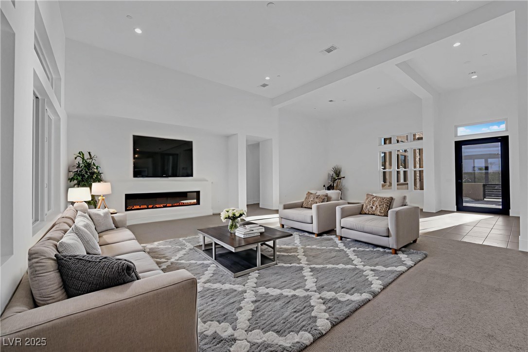 4792 Outlook Peak Street Las Vegas, NV 89135 - Photo 4 of 56 Living area featuring beam ceiling, a glass covered fireplace, carpet, recessed lighting, and tile patterned flooring