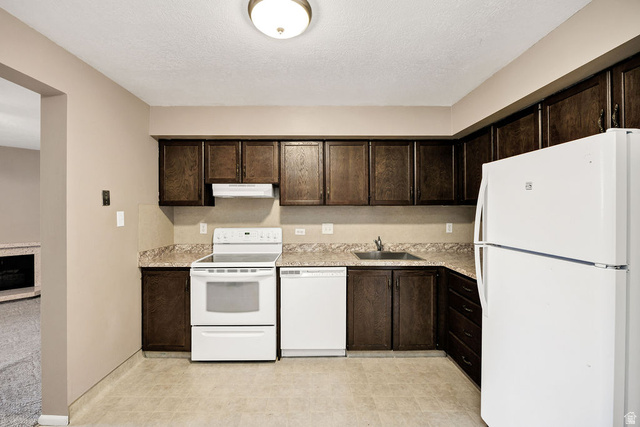 240 East 400 North, Unit 26 Logan, UT 84321 - Photo 3 of 12 Kitchen featuring dark wood-finish cabinetry, white appliances, and a laminate countertop
