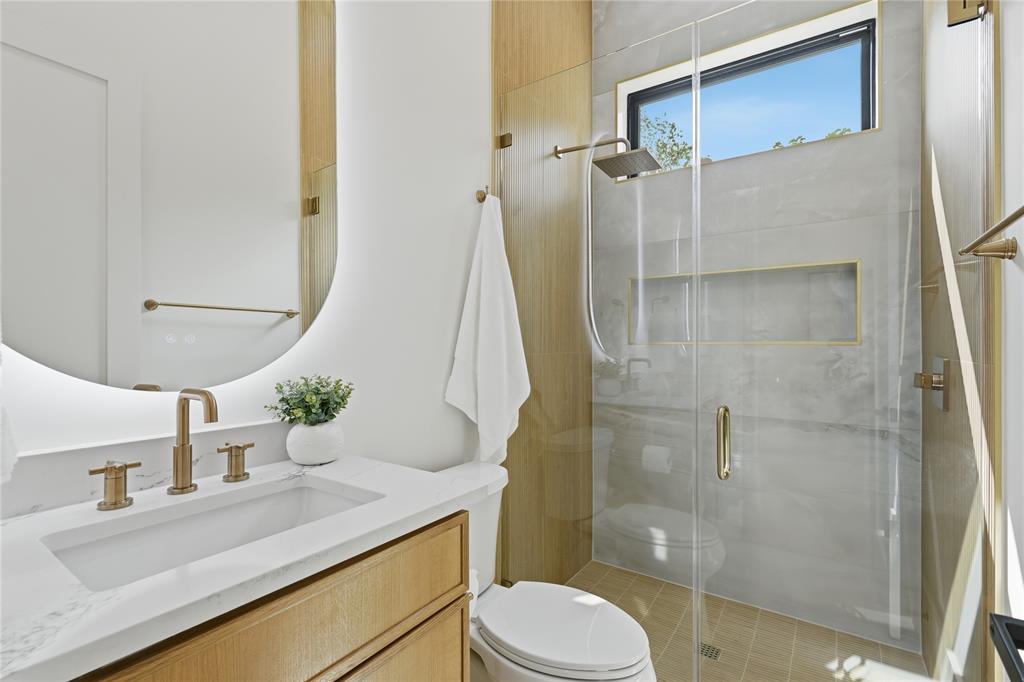6038 Prospect Avenue Dallas, TX 75206 - Photo 5 of 40 Bathroom featuring a wood-finish vanity with a white countertop and integrated sink, circular illuminated mirror, and brass-finish fixtures