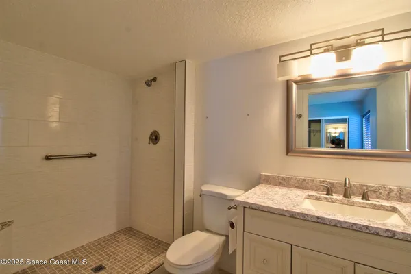 a bathroom with a granite countertop sink a toilet a mirror and shower
