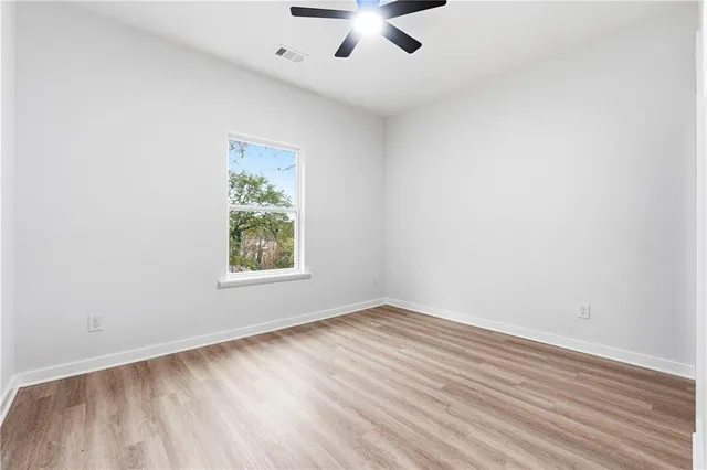 an empty room with wooden floor chandelier fan and windows