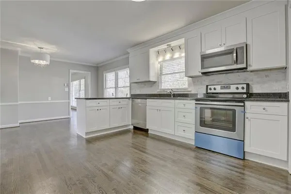 a kitchen with stainless steel appliances granite countertop white cabinets a sink a stove a microwave and wooden floors