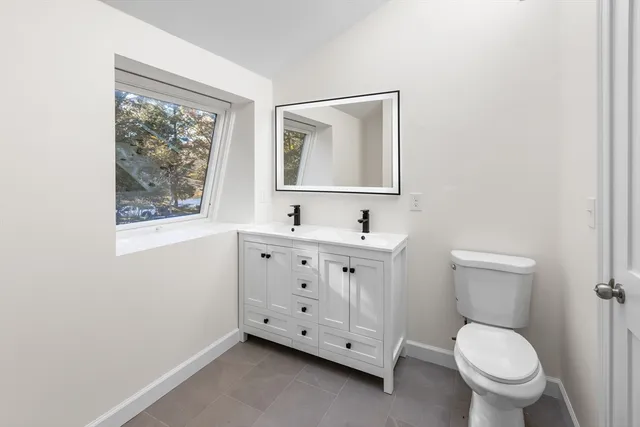 a bathroom with a toilet a sink a mirror and a window