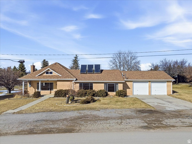 Ranch-style house with a front lawn, roof mounted solar panels, and driveway
