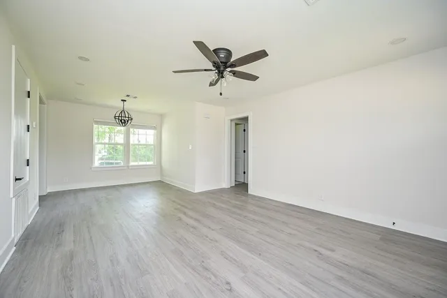 an empty room with wooden floor ceiling fan and windows