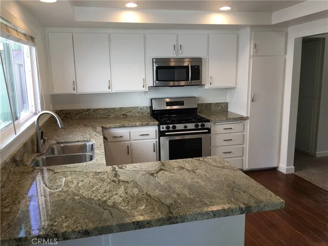 a kitchen with granite countertop a stove top oven a sink dishwasher and a refrigerator with wooden floor