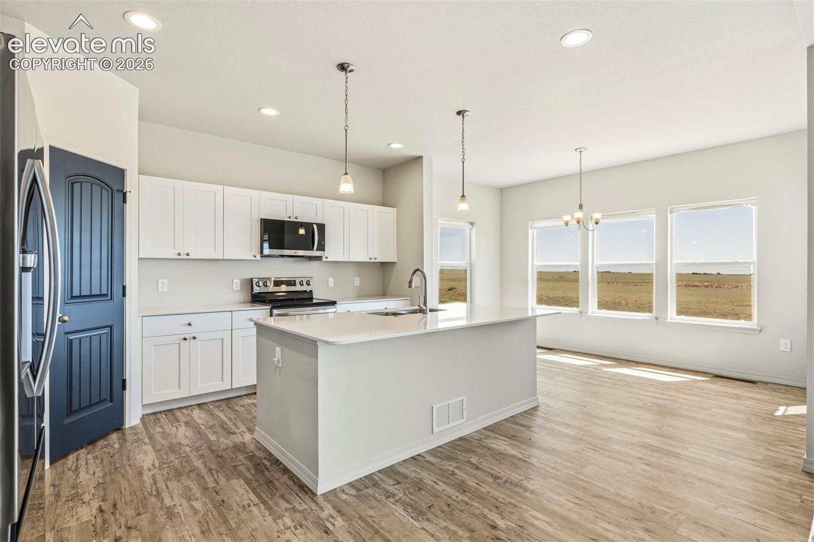 3955 North Yoder Road Yoder, CO 80864 - Photo 12 of 38 Open-concept kitchen featuring white shaker cabinetry, an island with an undermount sink, stainless steel appliances, and recessed lighting