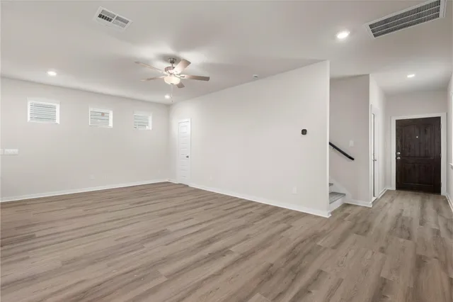 a view of an empty room with wooden floor and a ceiling fan