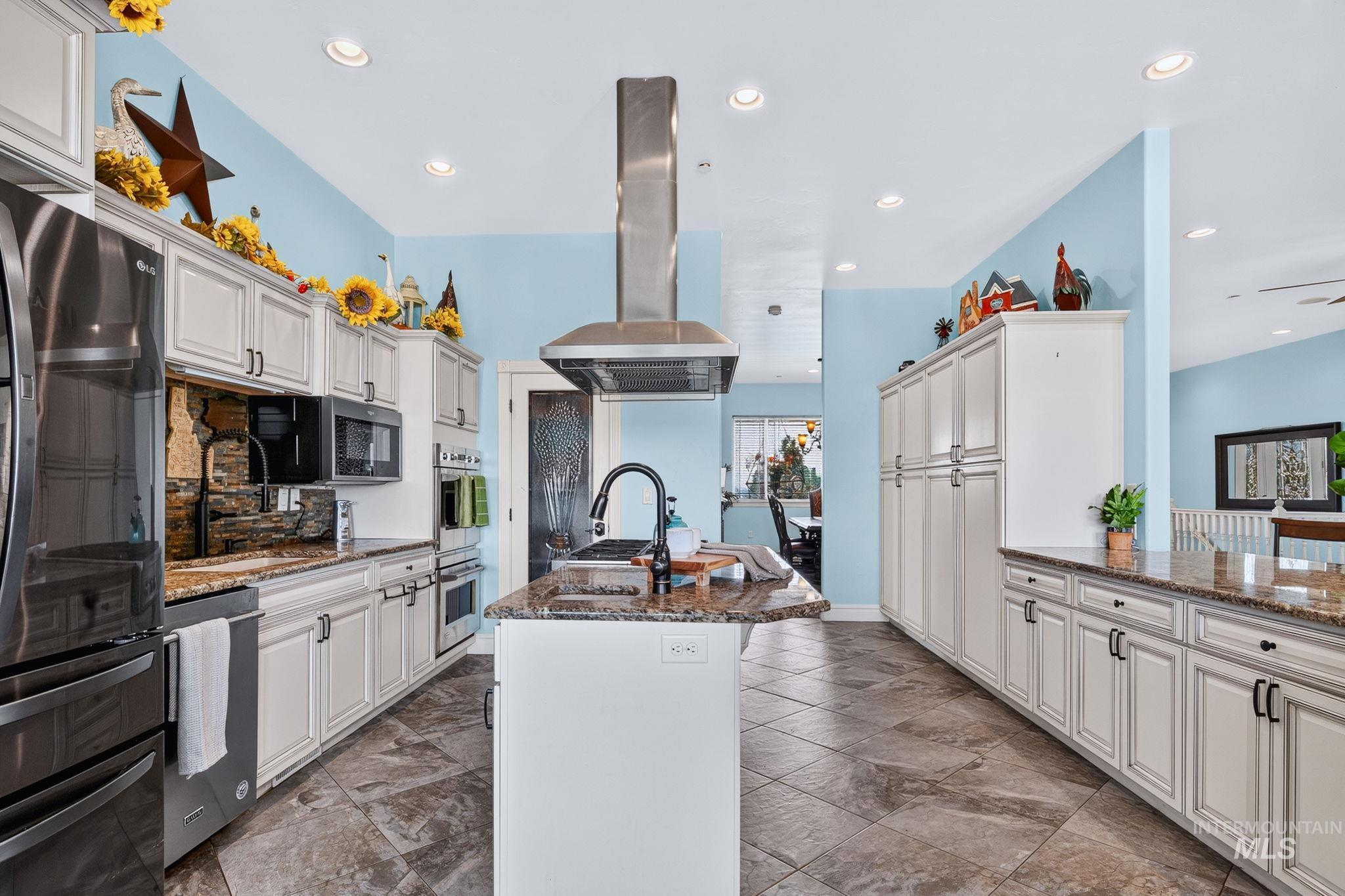 11378 Purple Sage Road Middleton, ID 83644 - Photo 11 of 50 Kitchen featuring a central island with an undermount sink and dark faucet, a professional-grade range with a stainless steel vent hood, light cabinetry, and granite countertops