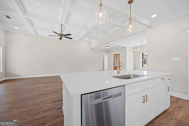 a kitchen with a sink dishwasher and white cabinets with wooden floor