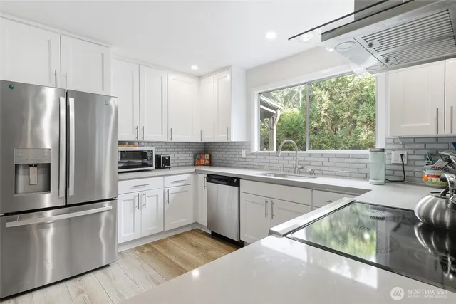 a kitchen with stainless steel appliances granite countertop a refrigerator a sink dishwasher a stove and white countertops with wooden floor