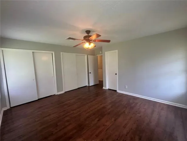 a view of an empty room with wooden floor and a ceiling fan