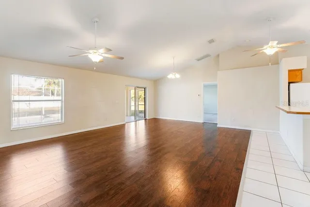 an empty room with wooden floor and a kitchen view