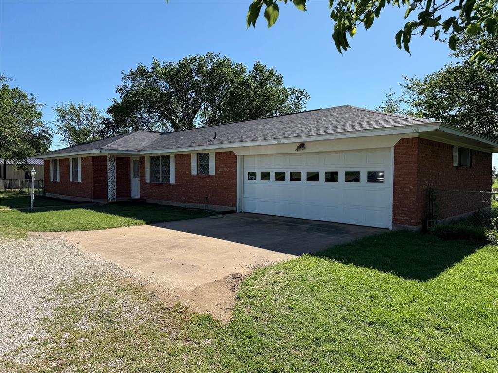 Ranch-style home with a front yard, a garage, driveway, brick siding, and fence