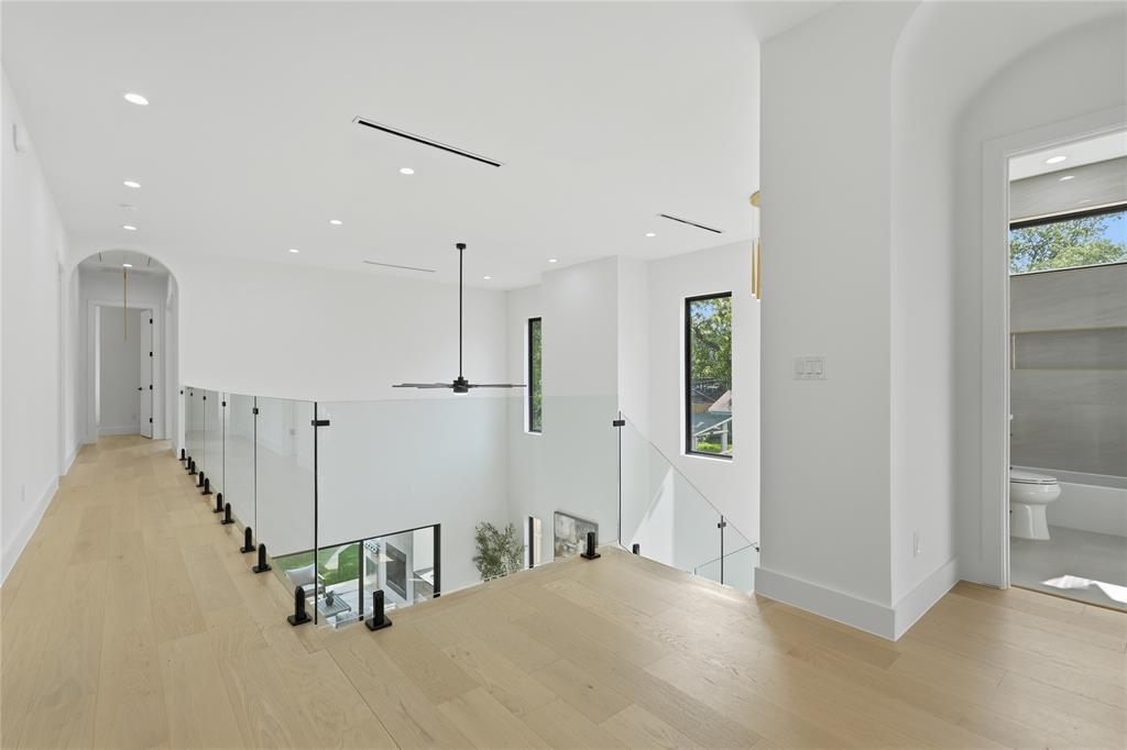 6038 Prospect Avenue Dallas, TX 75206 - Photo 27 of 40 Open loft area featuring light wood-finish flooring, a glass railing with black posts, recessed ceiling lighting, a contemporary black ceiling fan, and an arched hallway entry