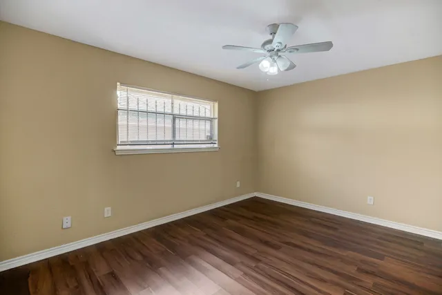 an empty room with wooden floor fan and windows