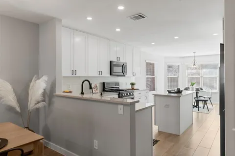 a kitchen with stainless steel appliances granite countertop a sink a stove a refrigerator cabinets and a dining table with wooden floor