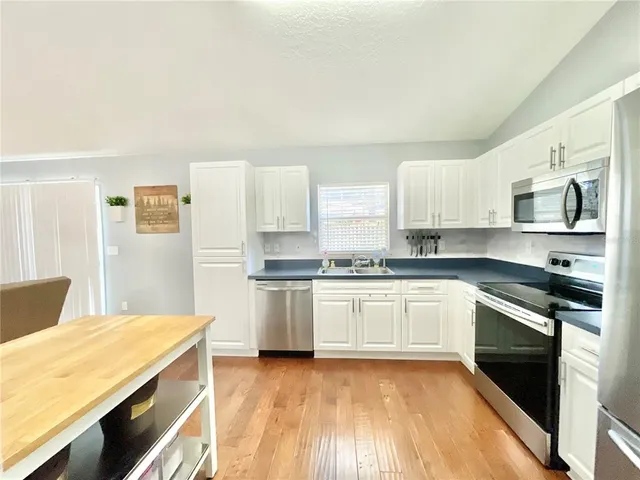 a kitchen with stainless steel appliances kitchen island granite countertop a refrigerator a stove and white cabinets with wooden floor