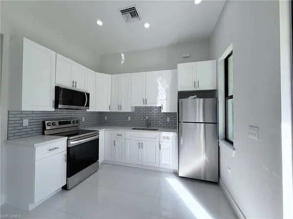 a kitchen with stainless steel appliances granite countertop a refrigerator a stove a microwave oven a sink dishwasher and white cabinets with wooden floor