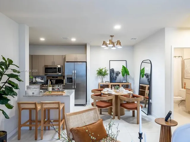 a kitchen with stainless steel appliances kitchen island granite countertop a refrigerator a stove a sink dishwasher and a dining table with chair