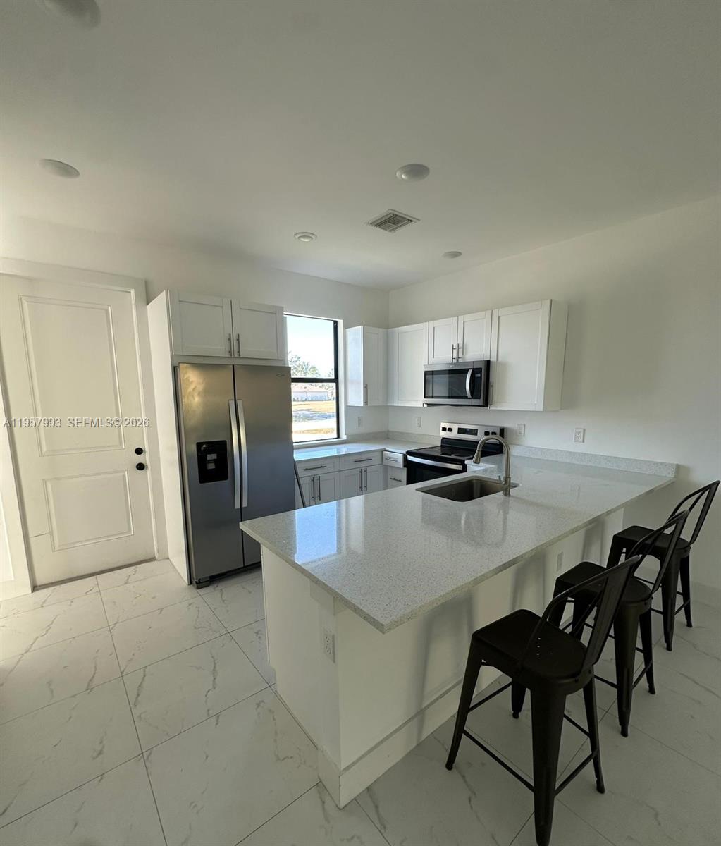 4660-4662 26th Street Southwest Lehigh Acres, FL 33973 - Photo 8 of 22 a kitchen with kitchen island a refrigerator stove microwave and cabinets
