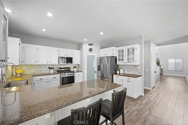 a kitchen with stainless steel appliances granite countertop a refrigerator a stove top oven a sink dishwasher and white cabinets with wooden floor