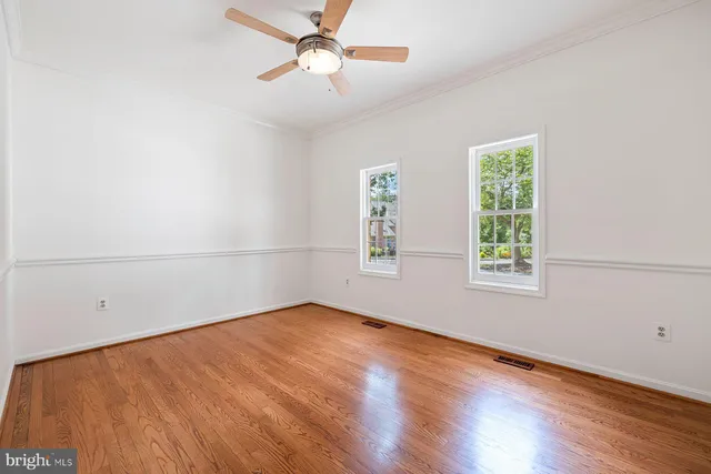 an empty room with wooden floor fan and windows