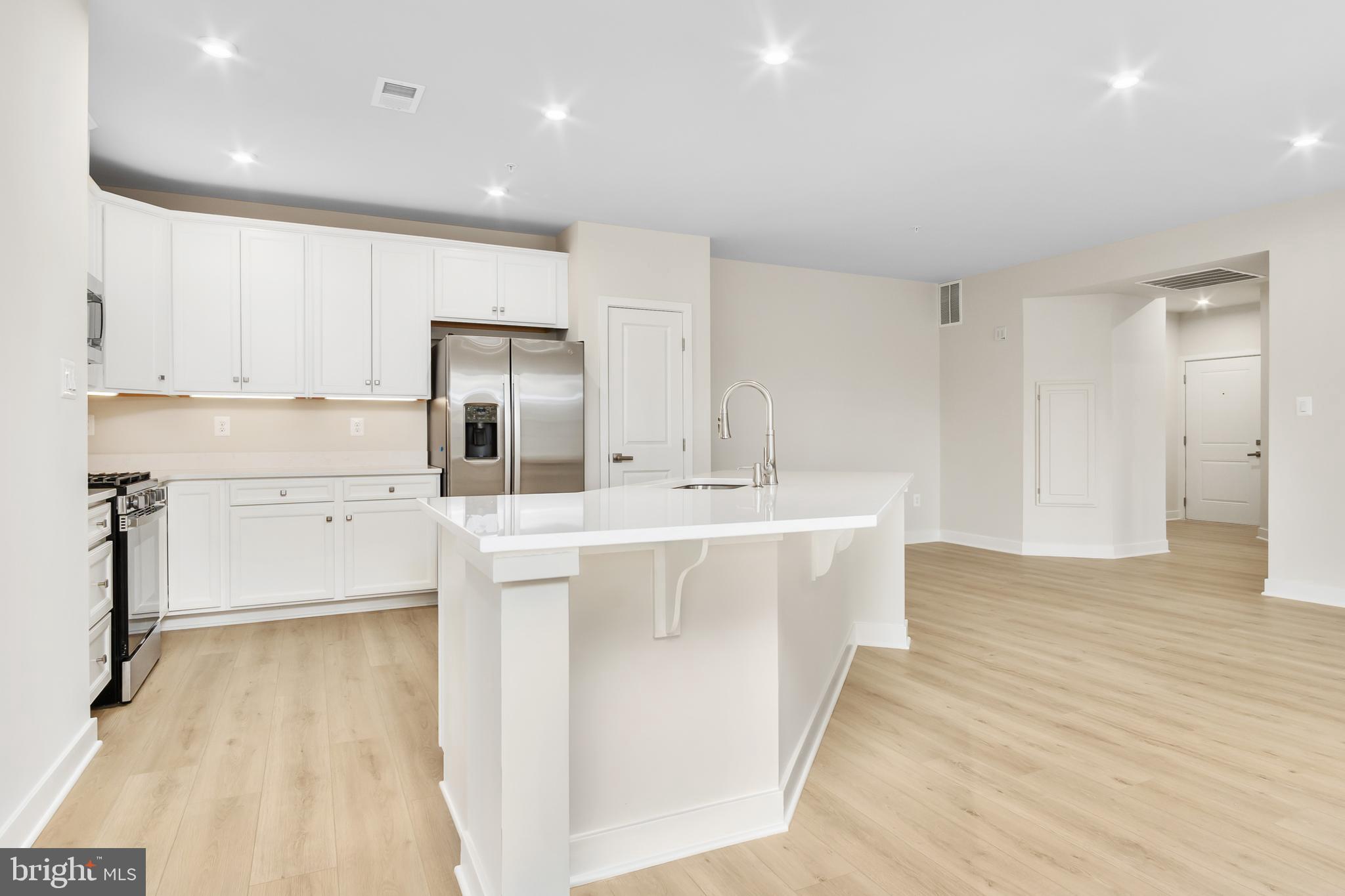 9935 Sofield Place, Unit 201 Frederick, MD 21701 - Photo 13 of 39 a large white kitchen with kitchen island a sink a stove and refrigerator