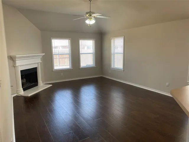 an empty room with wooden floor fireplace and windows