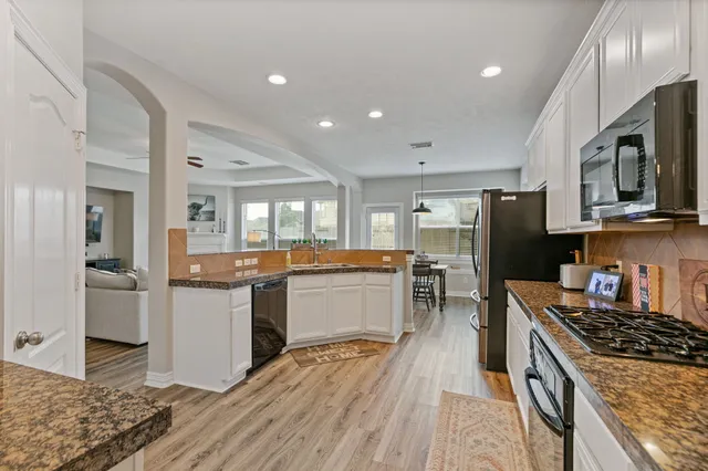 a kitchen with stainless steel appliances granite countertop a stove top oven a sink dishwasher a refrigerator and a dining table with wooden floor