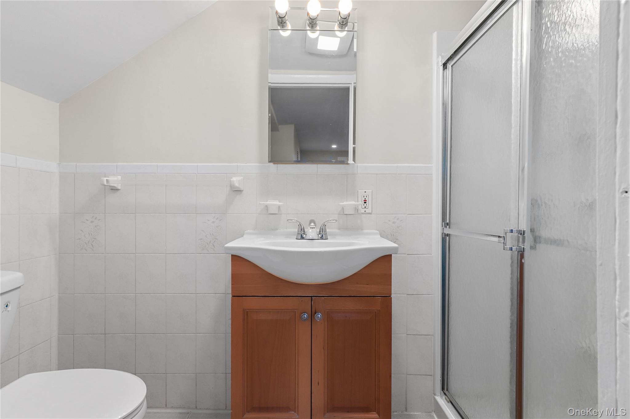 8 Virginia Avenue, Unit 1 Dobbs Ferry, NY 10522 - Photo 9 of 15 Bathroom featuring a stall shower, vanity, tile walls, a wainscoted wall, and lofted ceiling